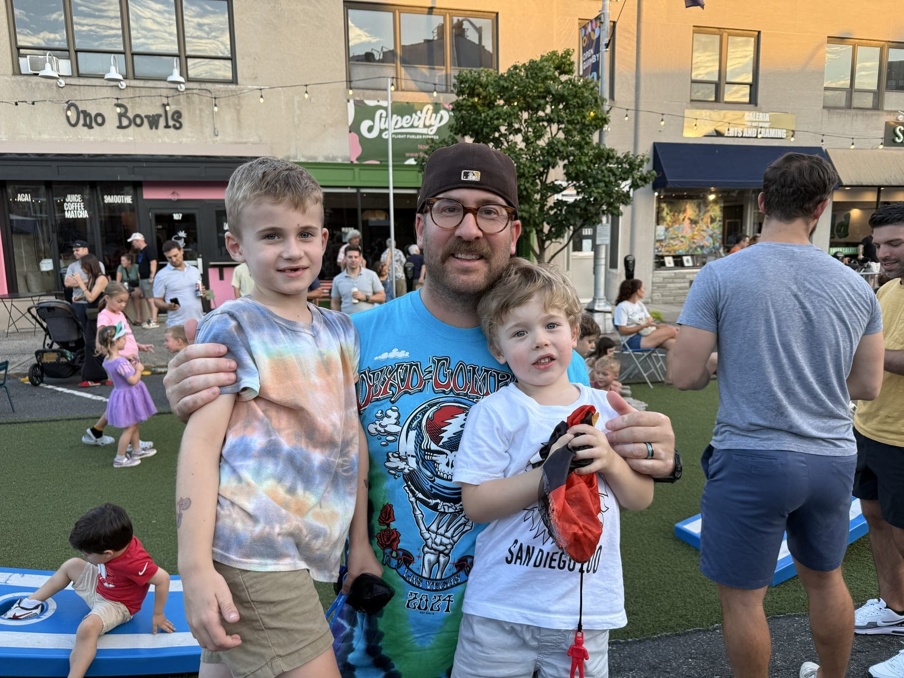 A father and his two sons enjoy the downtown atmosphere near the cornhole boards on Quimby Street.