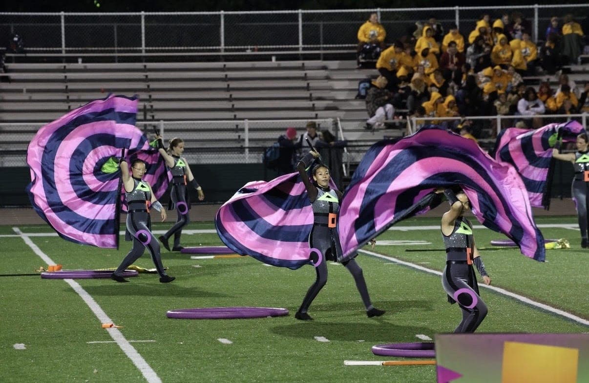 Color guard members spin oversized pink and navy flags during the band’s 2026 show, “In Shape.”