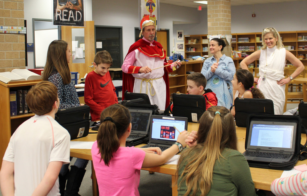 (above) Toga-clad sixth grade teachers Leslie Ortega (L) and Jennifer Benn look on as Alexander the Great (a.k.a. principal Robert Comba) visits a virtual ancient Greek agora (open air marketplace) created by their students. Photo Credit: Mary Ann McGann